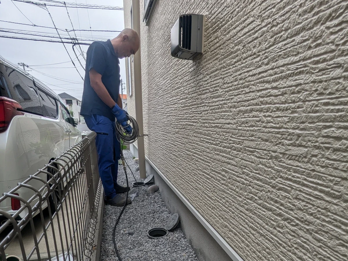 屋外の排水マスでホースを扱う代表・前田